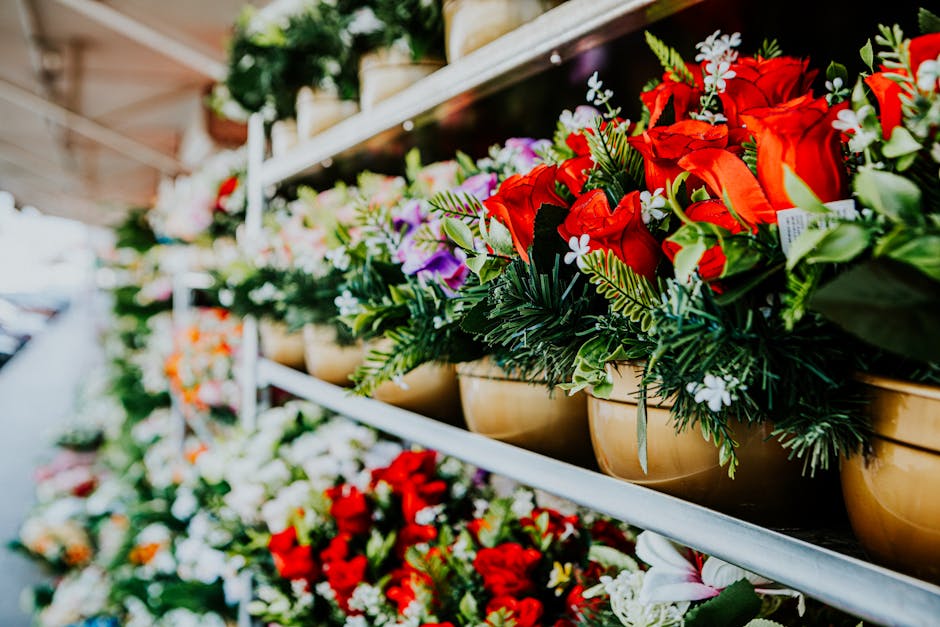 A row of beige ceramic bowls filled with an assortment of fresh floral arrangements, prominently featuring red roses, white and purple flowers, and lush green foliage. The bouquets are neatly arranged